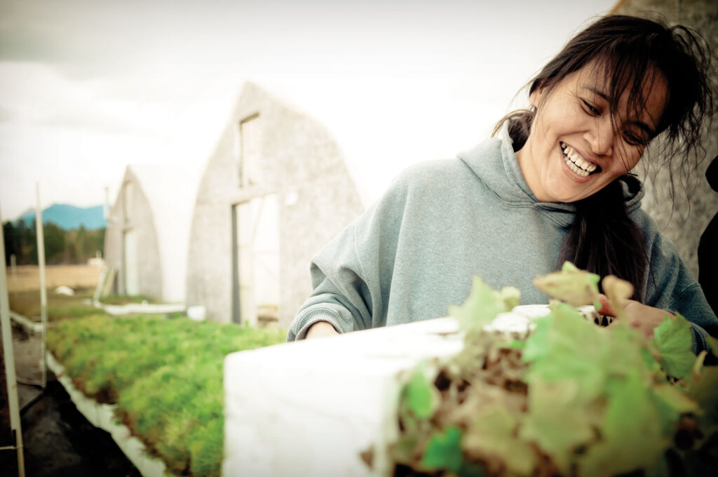 A woman smiling while working outside two greenhouse structures