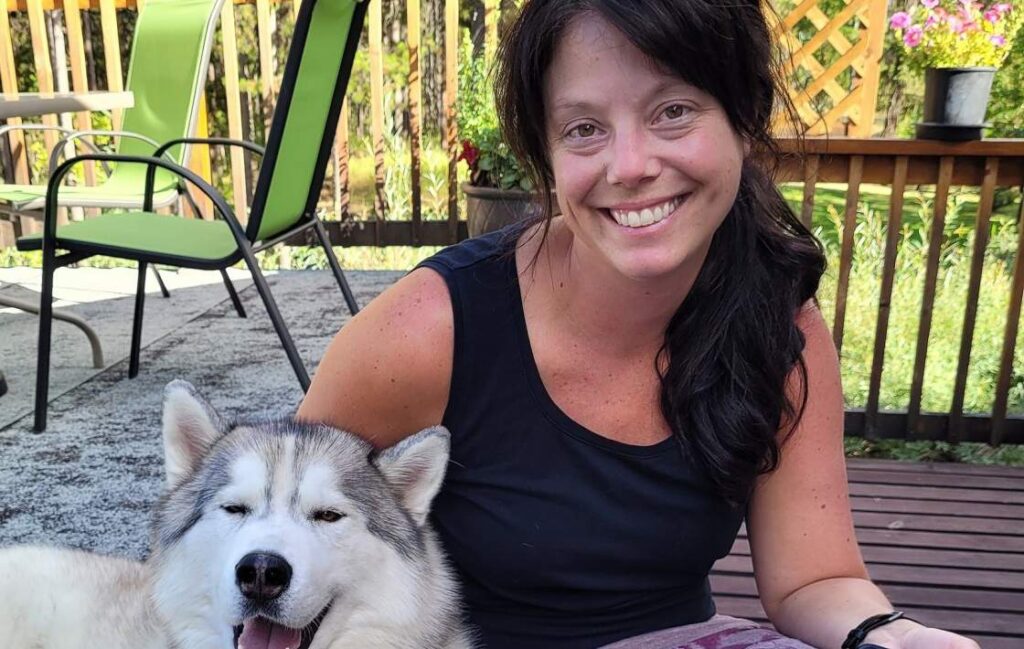 A woman sitting with a husky dog that looks content