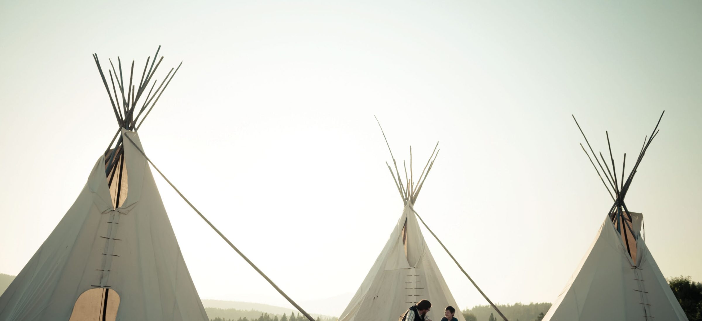 Two people sit at a picnic table in the center of three teepees.