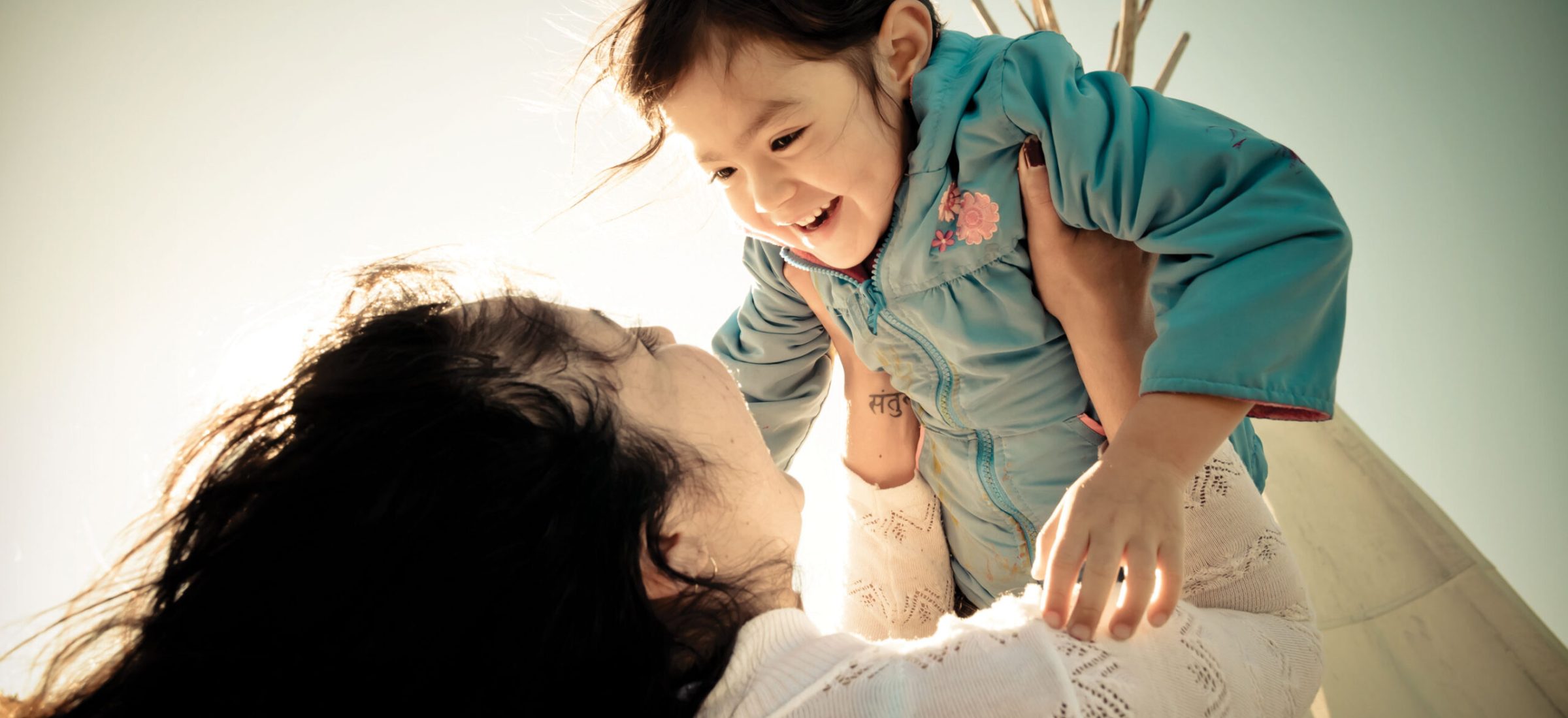 A woman holds up a child with a teepee in the background